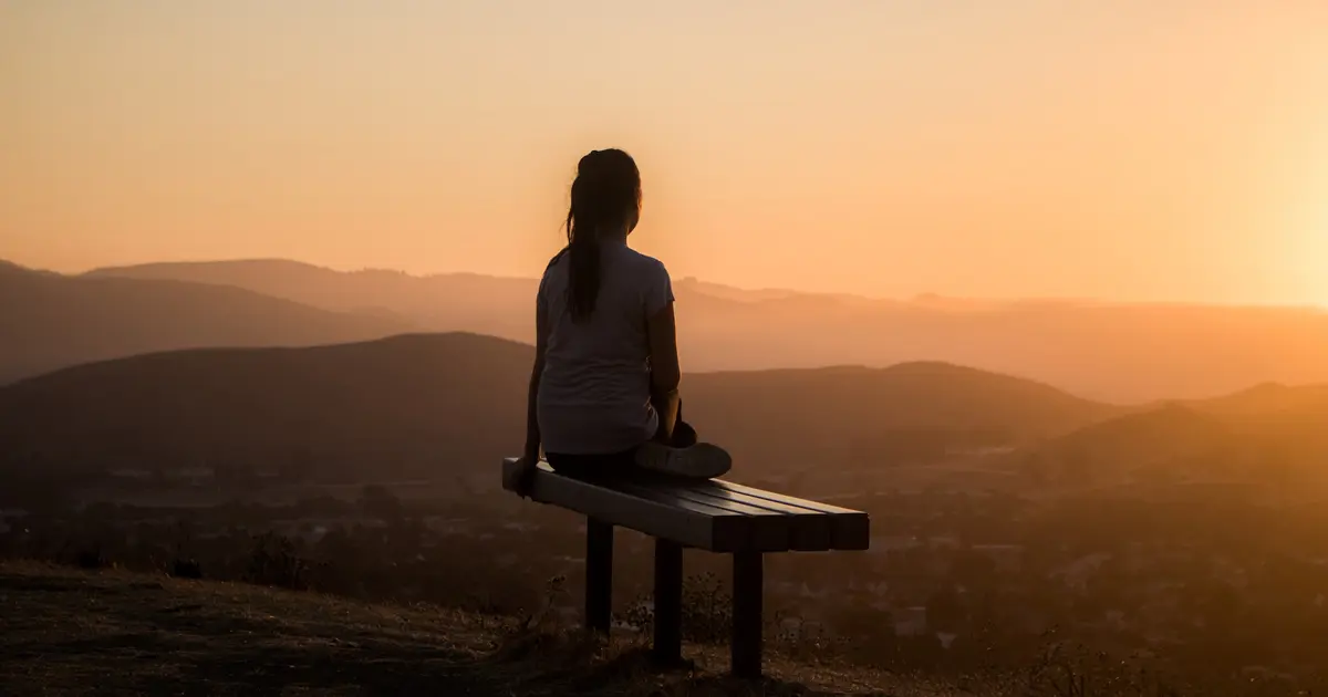 A woman sitting on a hillside bench