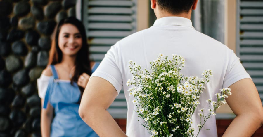man holding flower behind his back woman in front